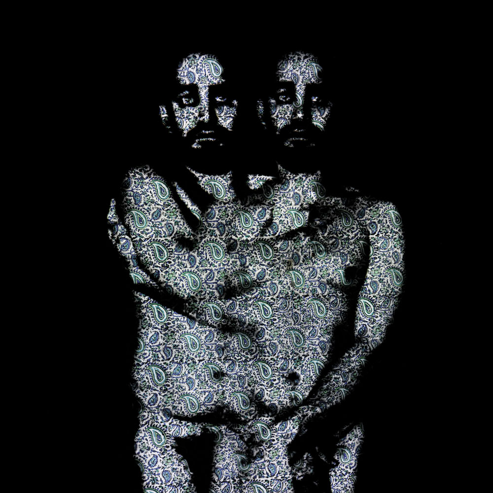 artwork in dark grey and blues with a paisley pattern duplicate image of two nude men